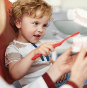 young boy playing with a toothbrush and a fake mouth