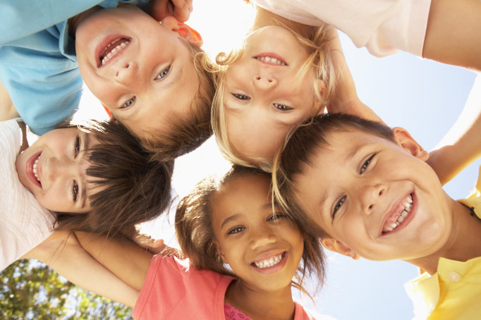 5 kids, boys and girls, look down at the camera while smiling on a sunny day getting ready to go back to school