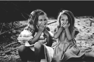 two young girls sitting holding their mouths shut with bad breath