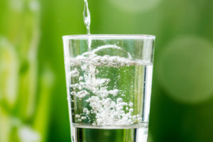 Clear glass of fluoridated water against a green background