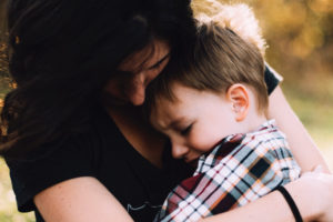 Brunette little boy is embraced by his mother while he cries due to sensitive teeth and tooth pain