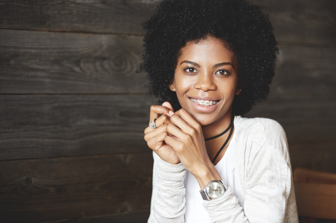 Curly-haired woman with adult braces smiles while wearing a white shirt