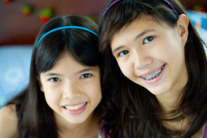 2 dark-haired smiling girls, one wearing braces