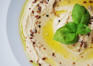 Aerial closeup of a plate of hummus topped with olive oil, seeds, and basil as a summer snack