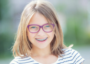 Blonde girl with braces and purple glasses smiles outside