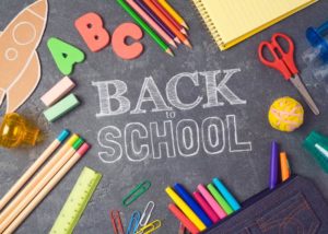Aerial view of a black chalkboard with the words BACK TO SCHOOL surrounded by various colorful school supplies
