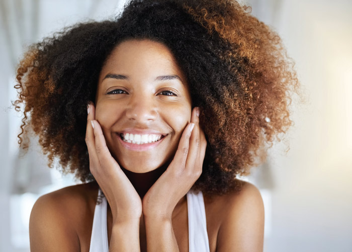 Brunette woman smiles and touches her cheeks after choosing between veneers and Lumineers