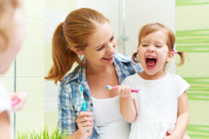 Mom makes brushing fun for her daughter in front of a green shower curtain in the bathroom