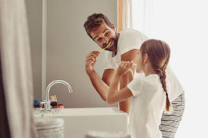 Dad & young daughter brushing their teeth together in front of the bathroom sink