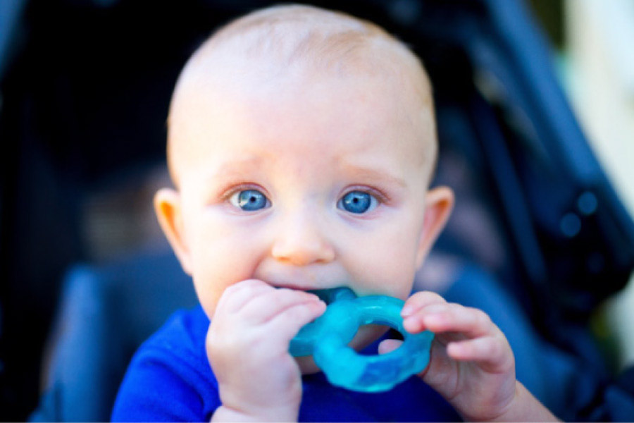 baby with blue eyes chews on a blue plastic rattle