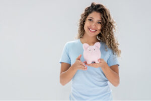 young woman holds a piggybank and smiles because of affordable dentistry