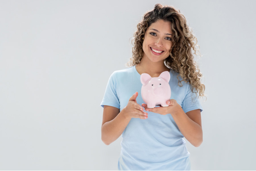 young woman holds a piggybank and smiles because of affordable dentistry