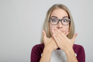 young woman wearing glasses covers her mouth to hide chronic bad breath