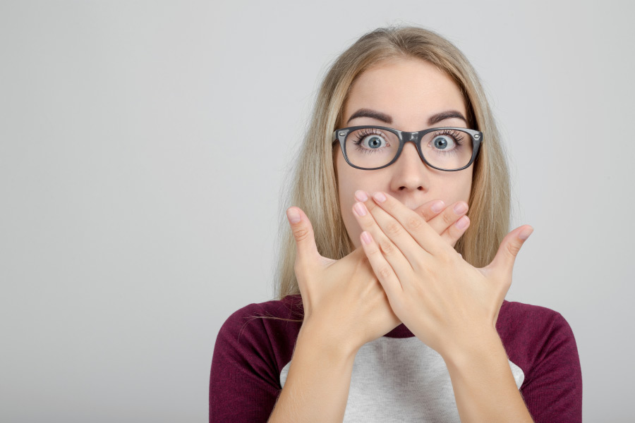 young woman wearing glasses covers her mouth to hide chronic bad breath