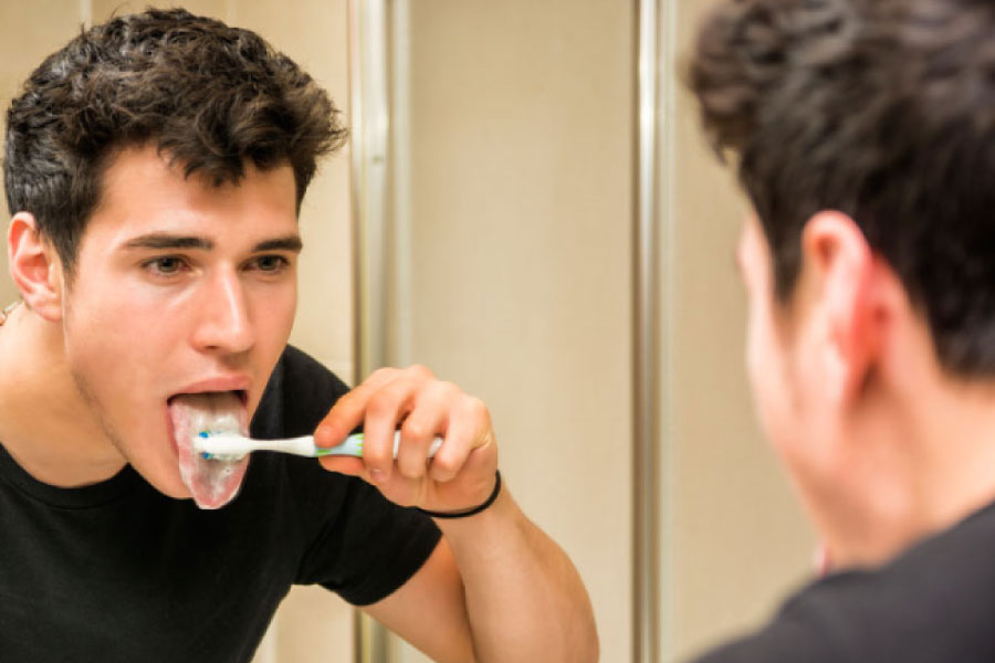 young man looking in a mirror brushing his tongue