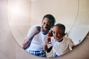 father and young son floss together in front of a mirror