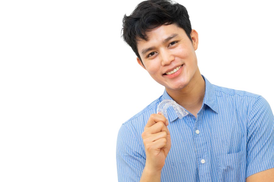 young man holds up his clear aligner and smiles showing off his straight teeth