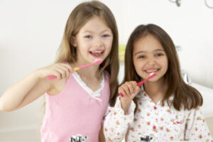two young girls brushing their teeth together.