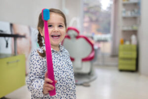 young girl holding a giant toothbrush at the dentist office